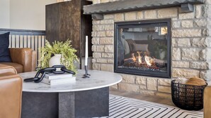 A cozy living area with a stone fireplace, leather sofa, and a round coffee table with books and a plant.