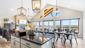 A spacious kitchen with a central island, a fireplace, and large windows offering a view of the outdoors.