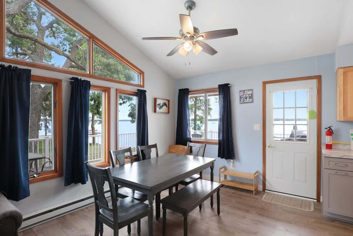 Un coin repas comprenant une table et des chaises, un ventilateur de plafond et de grandes fenêtres avec des rideaux.