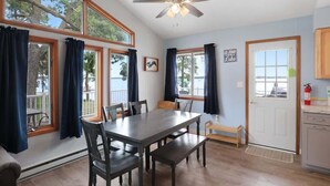 A dining area with a table and chairs, a ceiling fan, and large windows with curtains. - Amazing Grace Etta Shores (Henning)