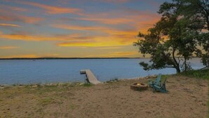 A lakeside setting with a fire pit and chairs, a concrete pathway leading to the water, and a tree providing shade. - Amazing Grace Etta Shores (Henning)
