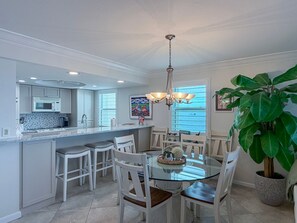 Une cuisine moderne avec des meubles blancs, un îlot central doté de sièges et un coin repas avec une table et des chaises en verre.