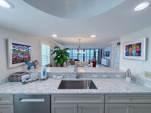 A modern kitchen with a marble countertop, stainless steel sink, and a dining area with a view.