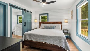 Une chambre à coucher avec un lit, deux lampes de chevet, un ventilateur de plafond et une fenêtre donnant sur un paysage verdoyant.