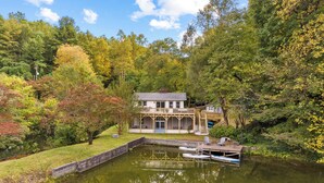 Une propriété au bord du lac, dotée d’un quai, d’une maison avec une terrasse et entourée d’arbres.