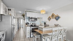 A modern kitchen with white cabinetry, a central island with seating, and a chandelier. - 3rd Floor Condo w/Amazing Ocean Views! Pool & Pier Access! In Heart of IOP! *Unit 321* (Isle Of Palms)