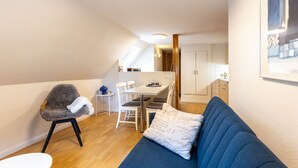Ein kompakter Wohnraum mit Essbereich, Küchenzeile und gemütlichem Sitzbereich mit Sofa und Sessel.
