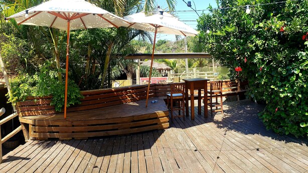 A wooden deck with seating and umbrellas, surrounded by lush greenery. - Pico da Tribo Pousada (Imbituba)