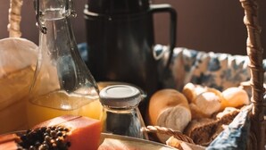 A wicker basket filled with breakfast items including bread, pastries, and a bottle of juice. - Pico da Tribo Pousada (Imbituba)