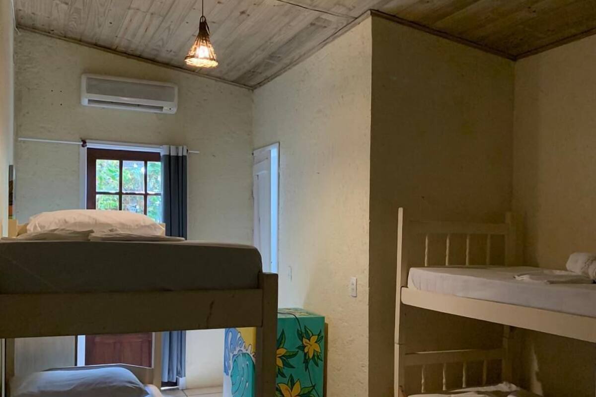 Une pièce avec deux lits superposés, une fenêtre avec des rideaux, une porte et une boîte verte ornée de motifs floraux.