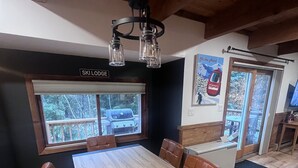 Ein Essbereich mit Holztisch und Ledersesseln, einer hängenden Leuchte und einem Fenster mit Blick auf eine Terrasse und einen Grill.