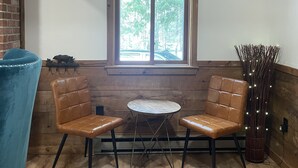 Ein Zimmer mit Holzwänden, einem Fenster mit Jalousien, zwei braunen Ledersesseln, einem kleinen runden Tisch und einer Zierpflanze.