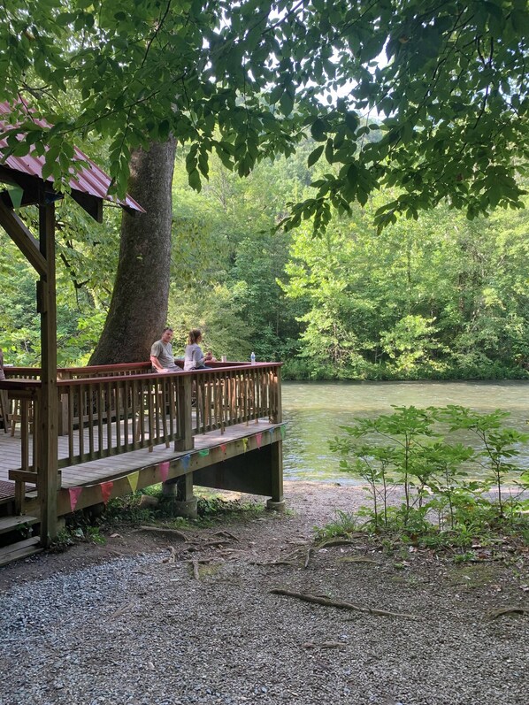 A wooden deck with a railing overlooking a body of water, surrounded by dense greenery.