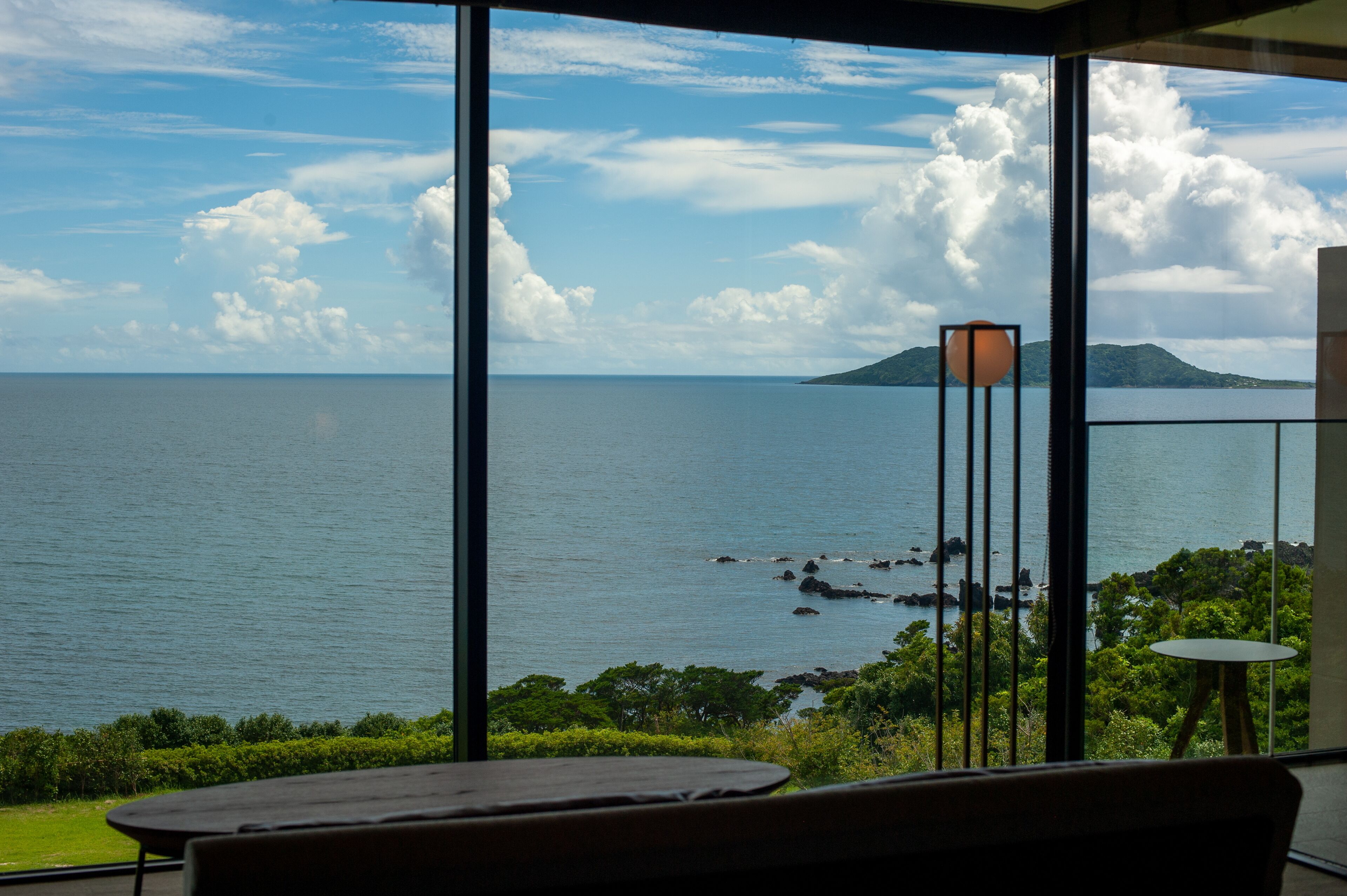 A view from a balcony overlooking a calm sea with distant land and a clear sky.