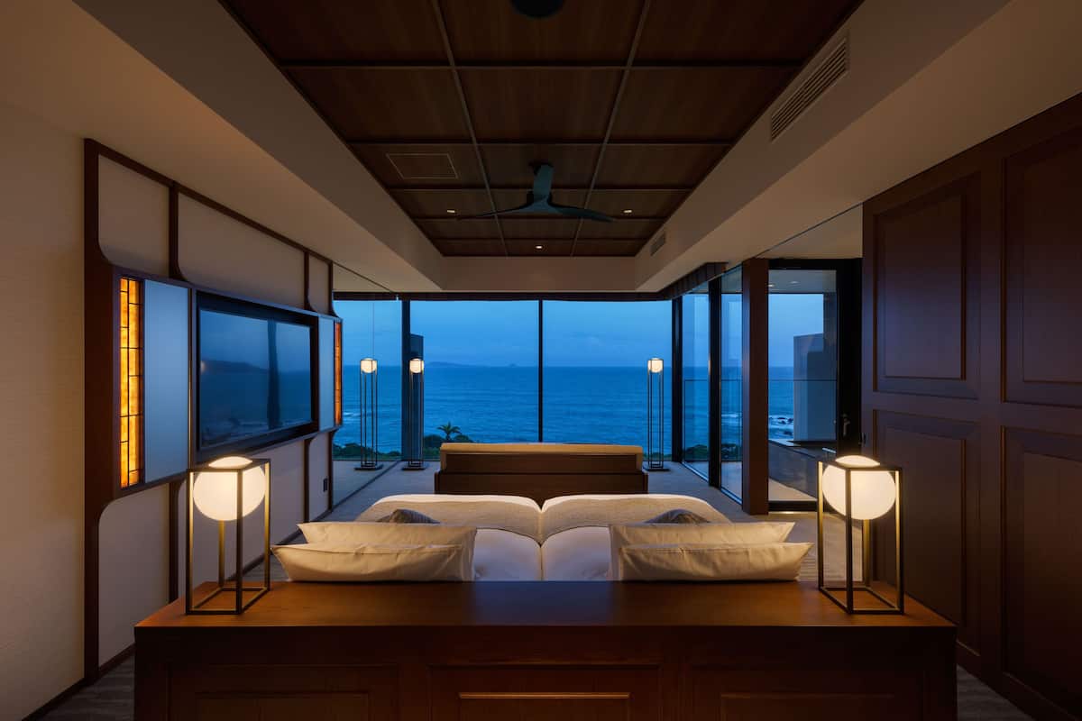 A bedroom with a large bed, bedside lamps, and a view of the ocean.