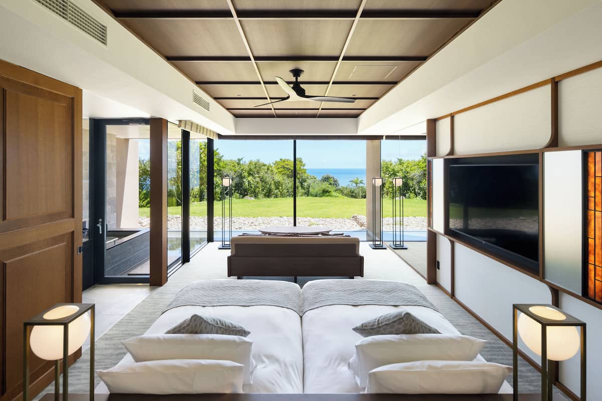 A modern bedroom with a large bed, a TV, and a view of the ocean.