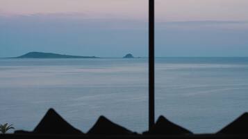 Vista a través de una ventana, con la silueta de una montaña al frente y un mar tranquilo con islas a lo lejos.