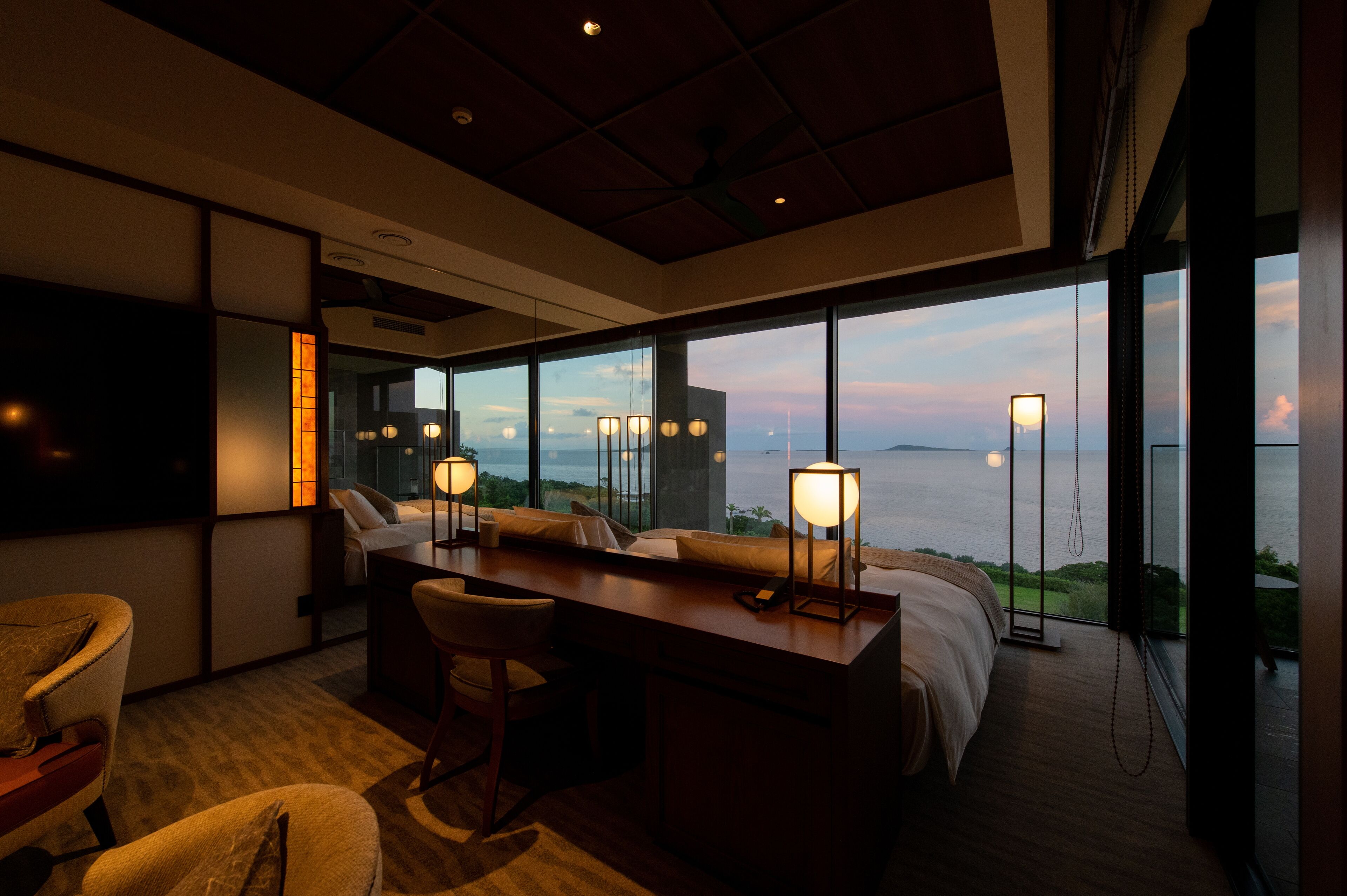 A modern hotel room with a large bed, a desk, and a view of the sea.