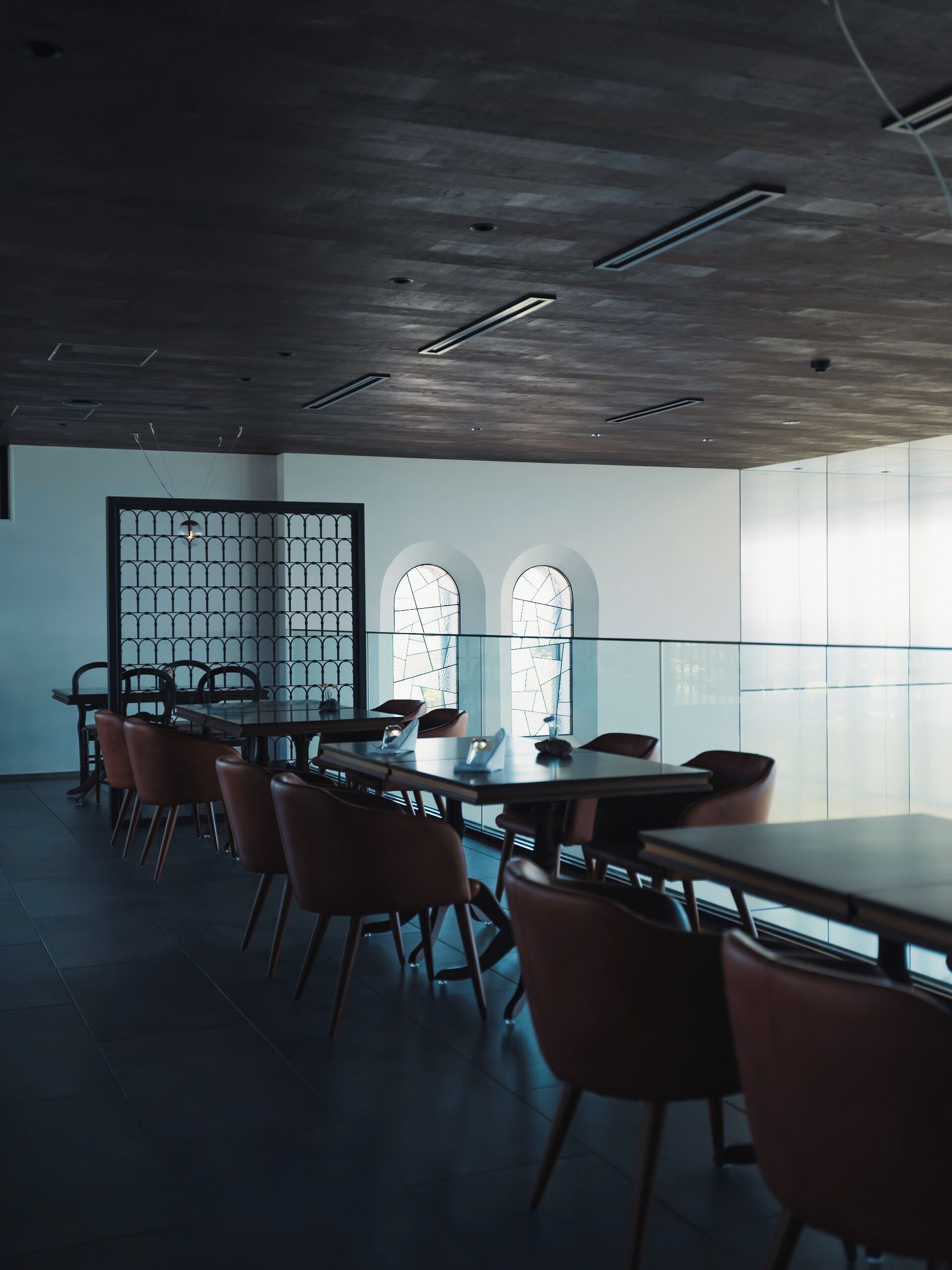 A modern conference room with a long table, multiple chairs, and large windows with arched tops.