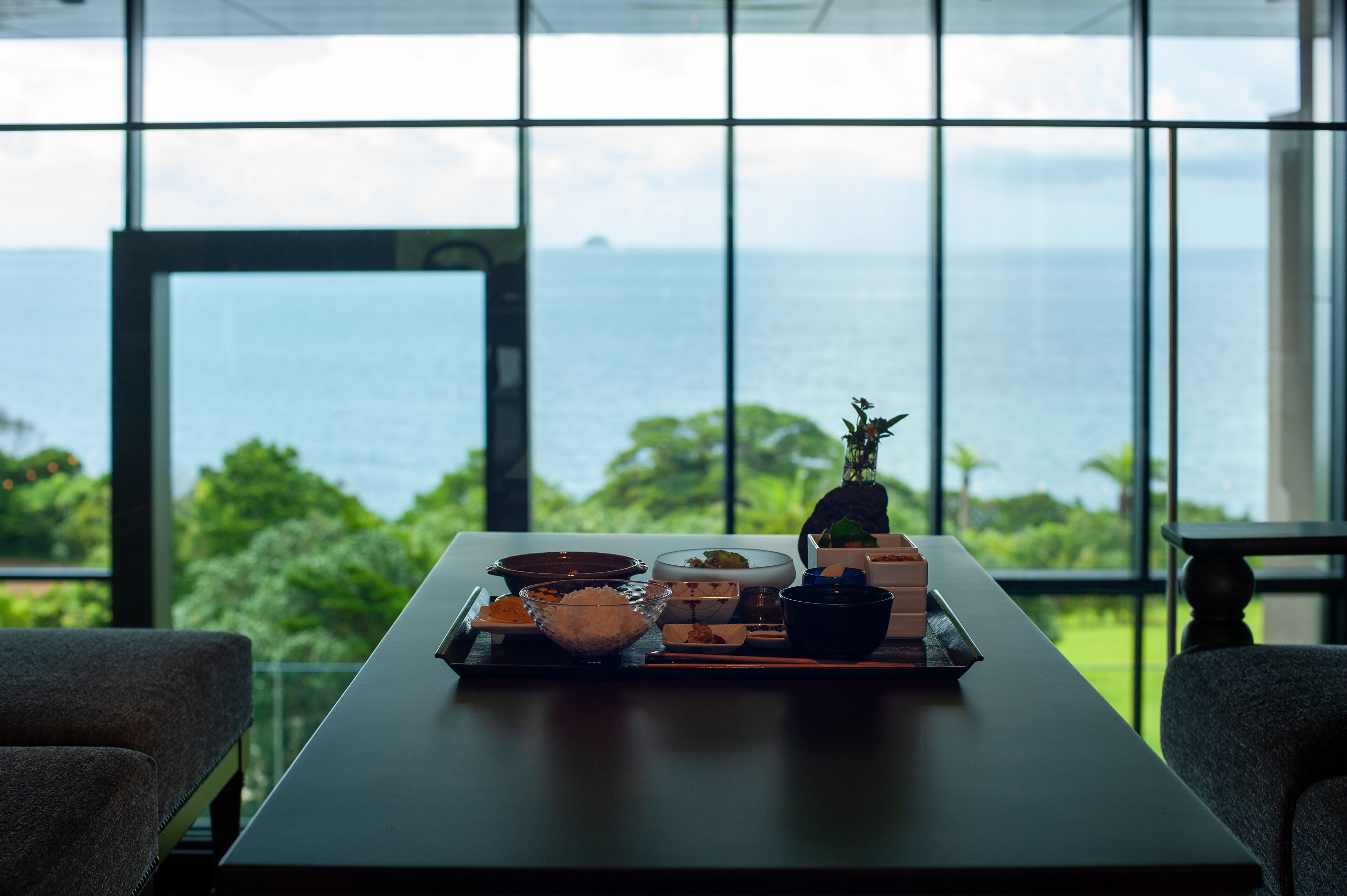 A dining table with various dishes and a view of the ocean through large windows.