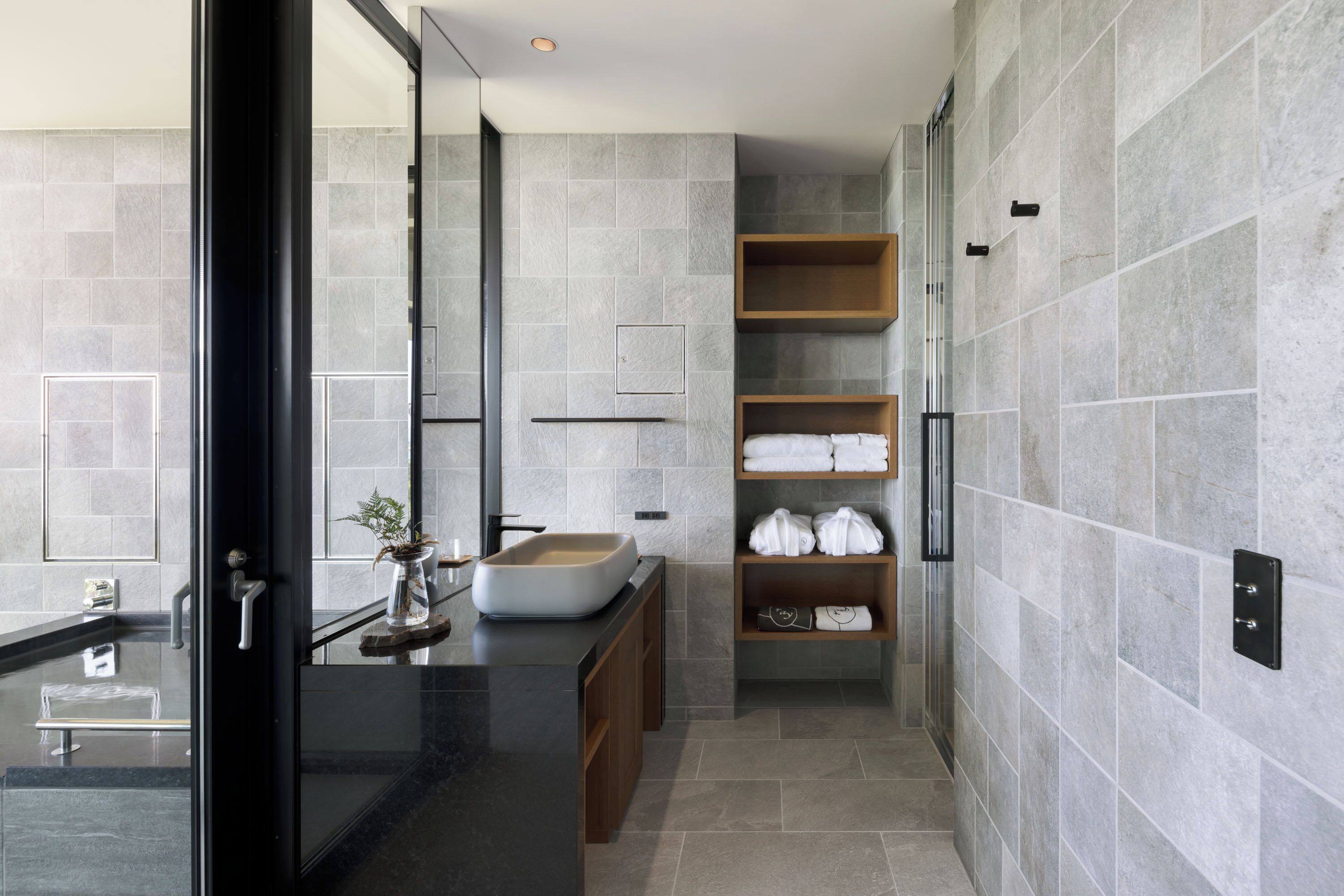 A modern bathroom with a glass-enclosed shower, a built-in sink, and a shelf with towels.