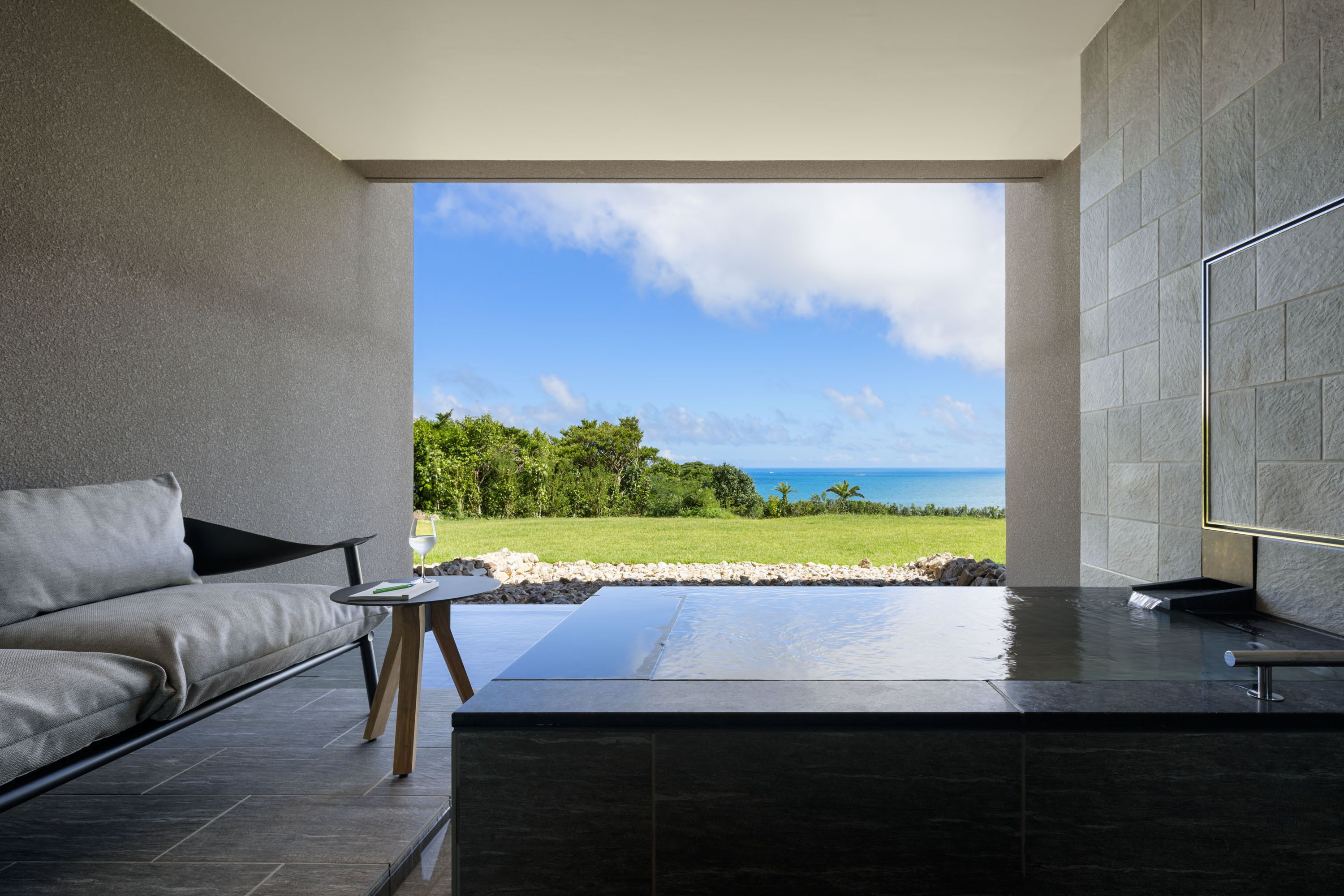 A modern bathroom with a large bathtub, a seating area with a sofa and table, and a view of the ocean.
