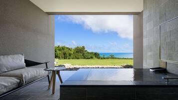 A modern bathroom with a large bathtub, a seating area with a sofa and table, and a view of the ocean.