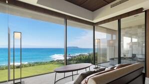 A modern living room with a large glass wall offering a view of the ocean. - GOTO RETREAT by Onko Chishin (Goto)