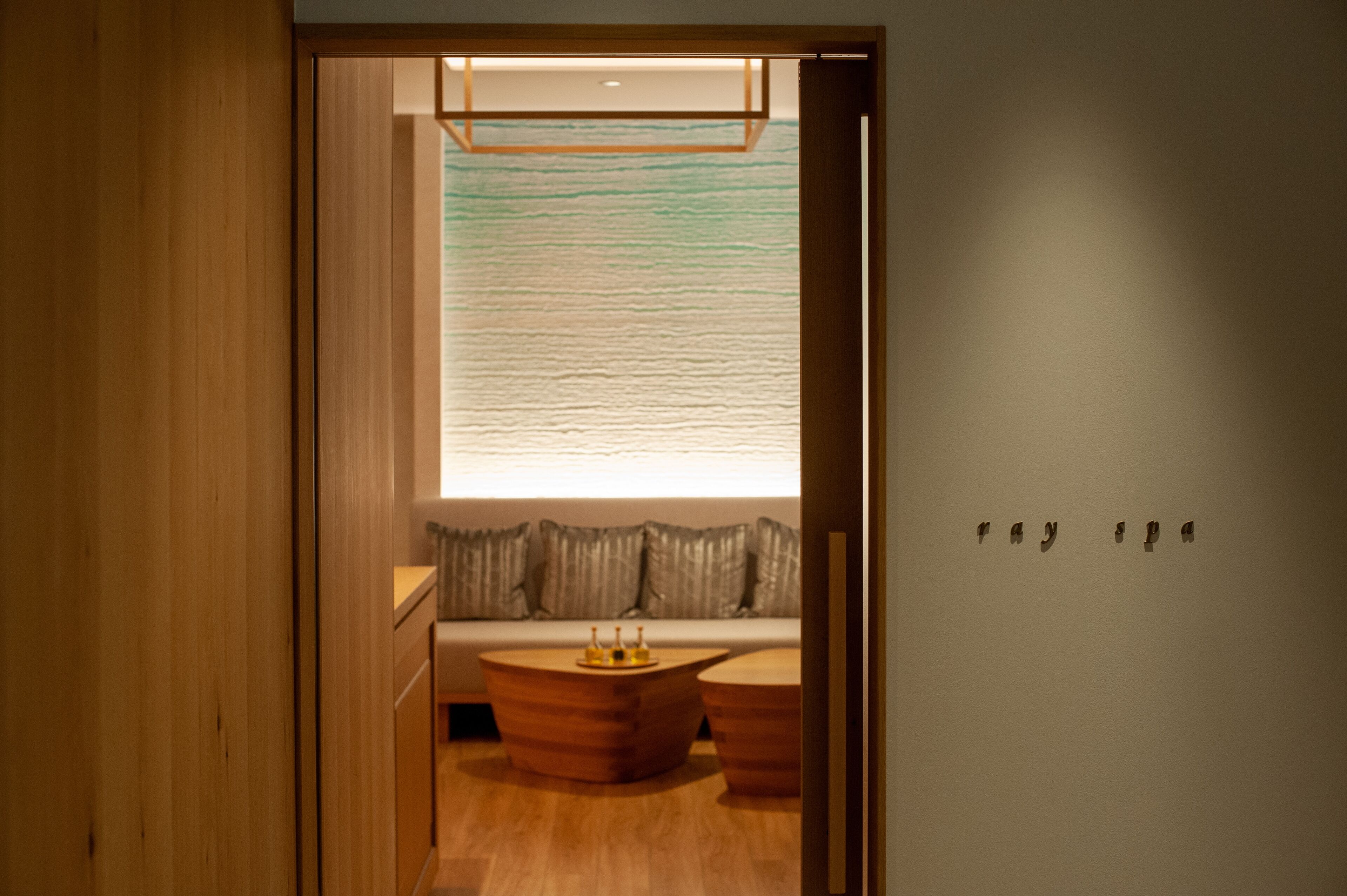 A modern room with a wooden floor, a sofa, two wooden side tables, and a large window with a view.