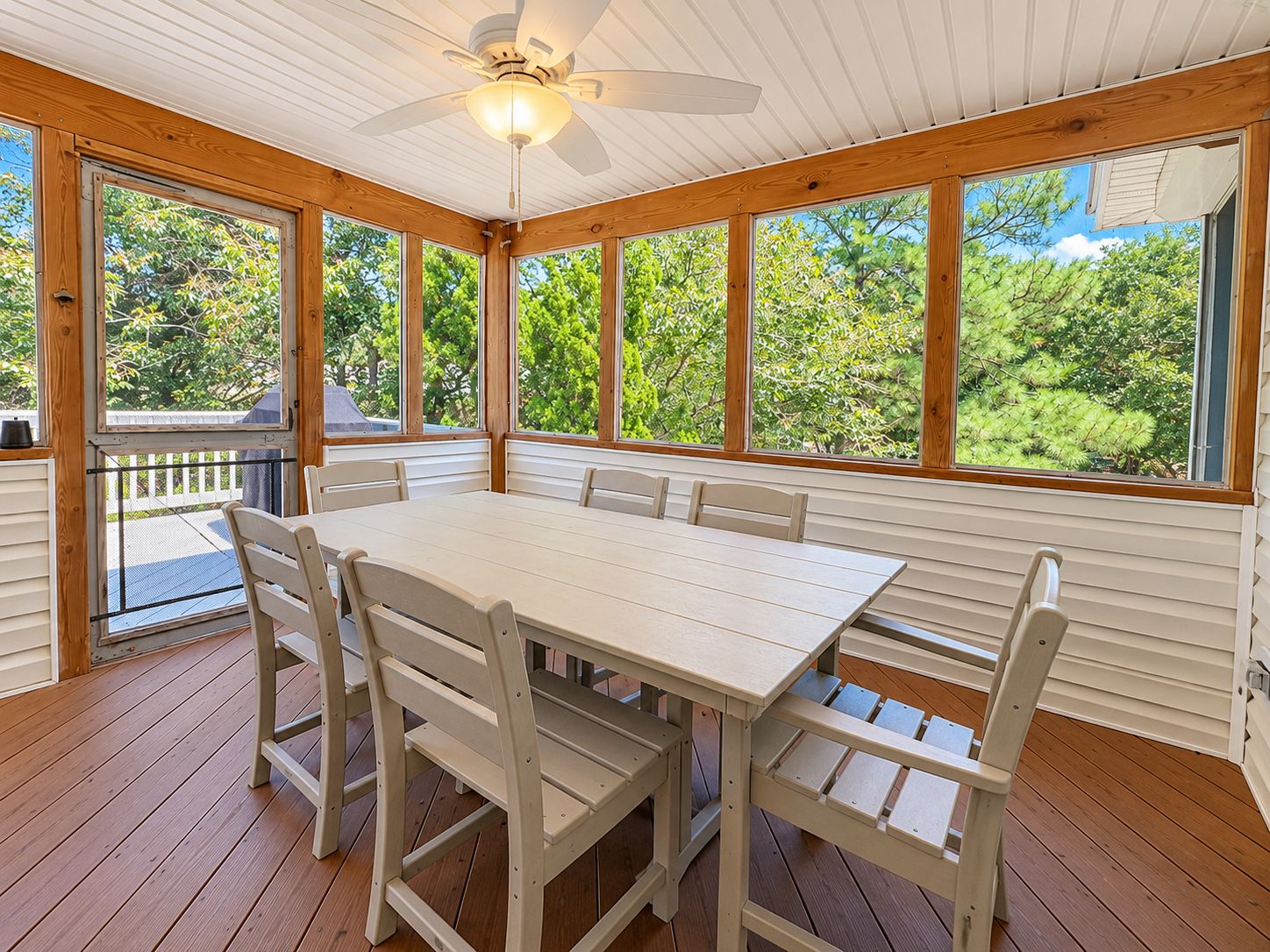 A covered outdoor dining area with a table and chairs, large windows, and a ceiling fan.