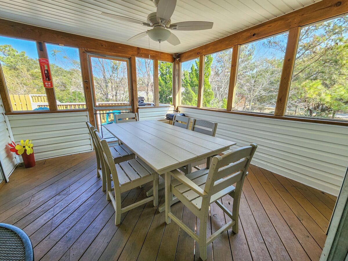 Eine überdachte Terrasse mit Holztisch und -stühlen, großen Fenstern und einem Deckenventilator.
