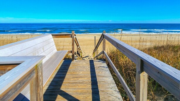 A wooden boardwalk leading to a beach with a clear view of the ocean.