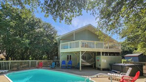 A swimming pool with a covered deck area, outdoor seating, and a building with a balcony.