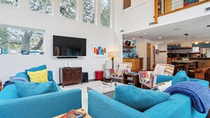 Een ruime woonkamer met een grote televisie, blauwe banken en een eethoek met een houten tafel.