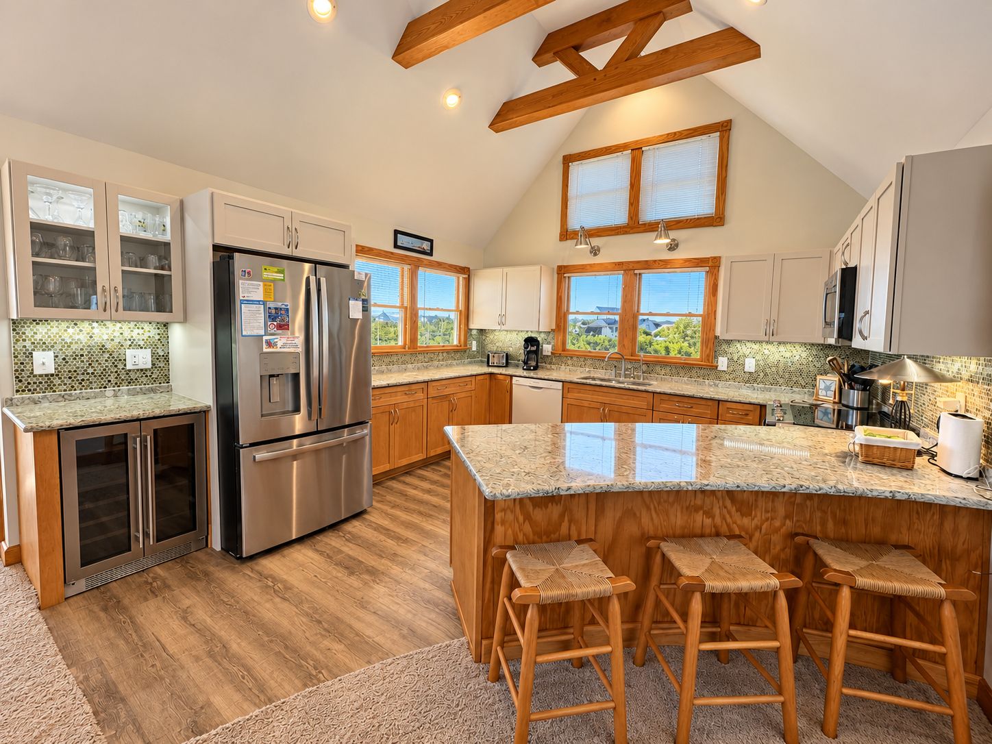 A kitchen with a large island, wooden bar stools, and a view of the outdoors through windows.