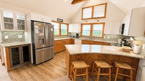 A kitchen with a central island, wooden stools, a stainless steel refrigerator, and wooden cabinets.