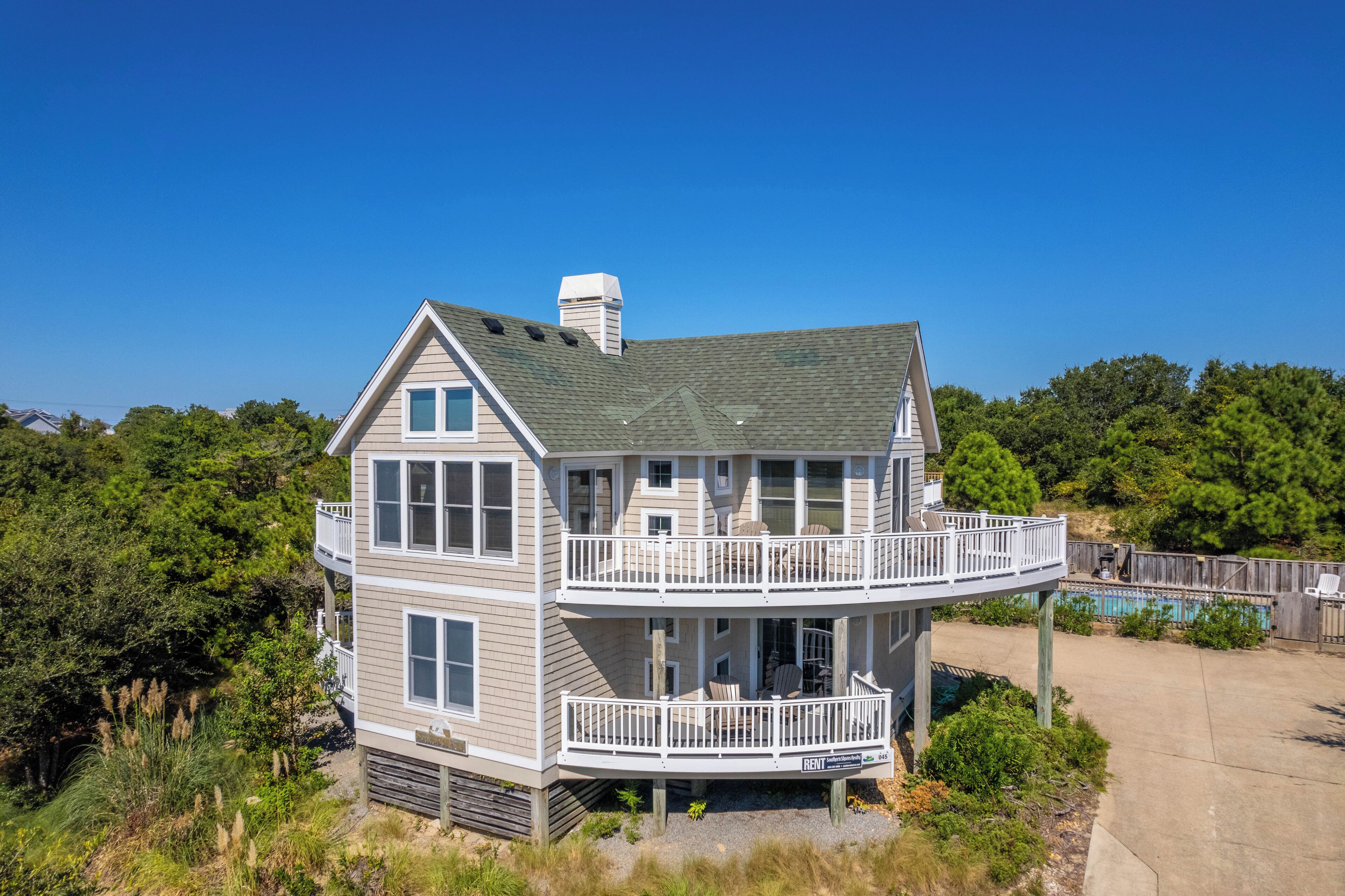 A two-story house with a balcony and a deck, surrounded by greenery.