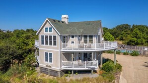 A two-story house with a balcony and a deck, surrounded by greenery.