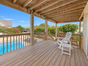 A wooden deck with a pool, white chairs, and a view of the neighborhood.