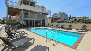 A pool area with lounge chairs and a two-story building with balconies. - The Penny Swan - Wake up to beautiful ocean views from this oceanside 7BR home w/Private Pool! (Southern Shores)