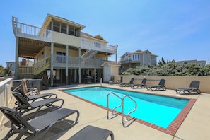 A pool area with lounge chairs and a two-story building with balconies. - The Penny Swan - Wake up to beautiful ocean views from this oceanside 7BR home w/Private Pool! (Southern Shores)