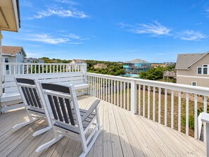 A wooden deck with a white railing, overlooking a residential area with houses and a swimming pool.