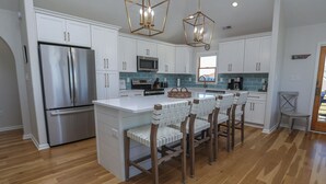 A modern kitchen with white cabinets, stainless steel appliances, and a central island with bar stools. - The Penny Swan - Wake up to beautiful ocean views from this oceanside 7BR home w/Private Pool! (Southern Shores)