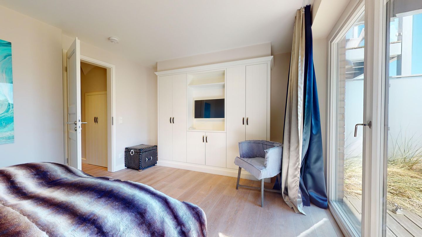 A bedroom with a bed, a chair, a wardrobe, and a window with curtains.