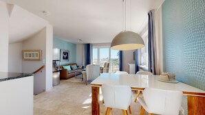 Een moderne woonkamer met een eethoek, met een grote tafel, witte stoelen en een hangende lamp.