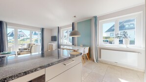 Een moderne keuken met een granieten aanrechtblad, witte kastjes en uitzicht op de buurt door grote ramen.