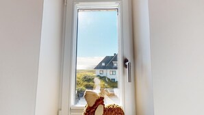 Une fenêtre donnant sur une maison, avec un ours en peluche posé sur le rebord.