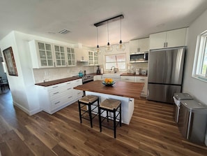 A modern kitchen with white cabinets, a central island, stainless steel appliances, and a wooden floor.