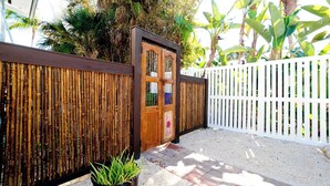 Un área cercada con valla de madera, portón metálico y una planta en maceta.