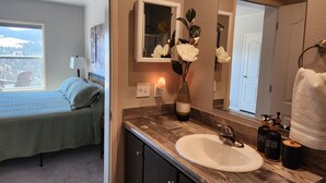 A bathroom with a wooden vanity, a white sink, and a mirror. There is a vase with flowers on the vanity. - Grandview Getaway offers spectacular views overlooking the Clearwarter river. (Lenore)